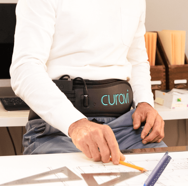A middle aged man sitting at work wearing a Curavi Belt for pain relief