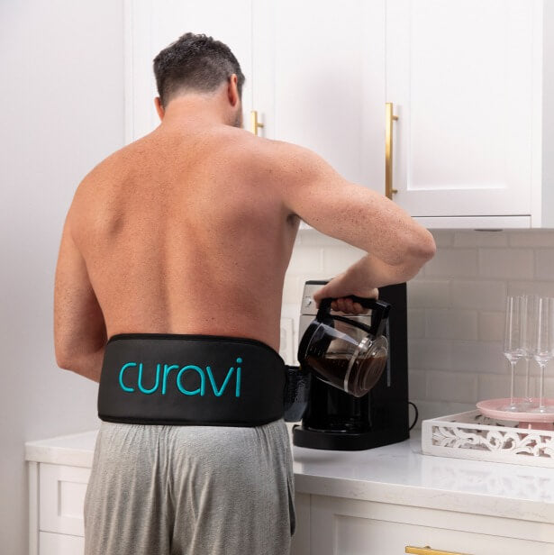 A young man using a Curavi Belt in his house while getting a cup of coffee